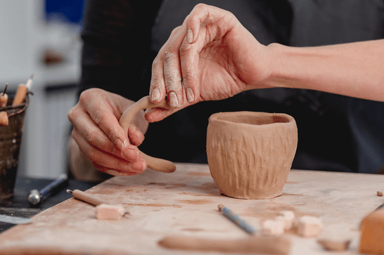 A person is moulding the handle of a mug, next to a textured mug cylinder