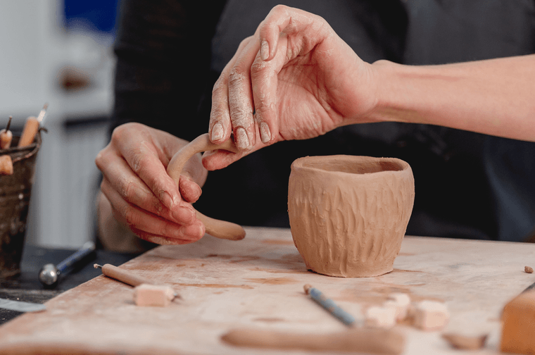 A person is moulding the handle of a mug, next to a textured mug cylinder
