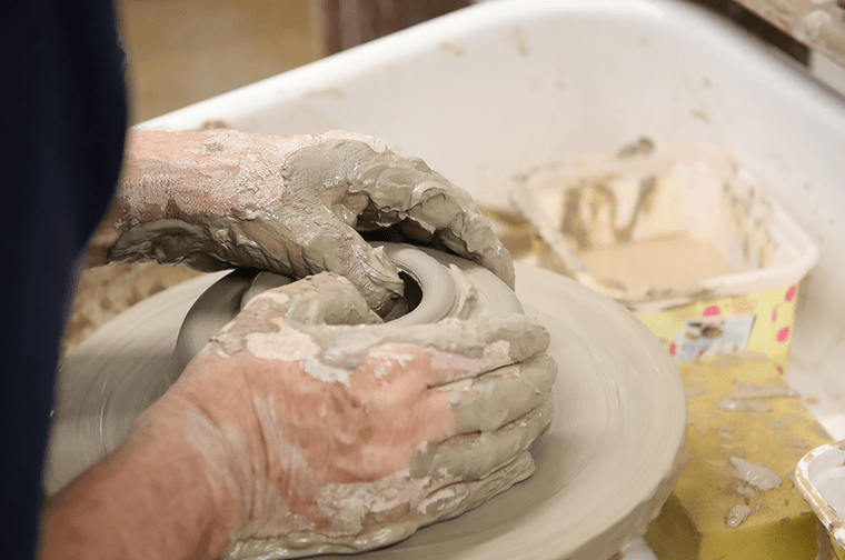 A person's hands are forming clay on a pottery wheel