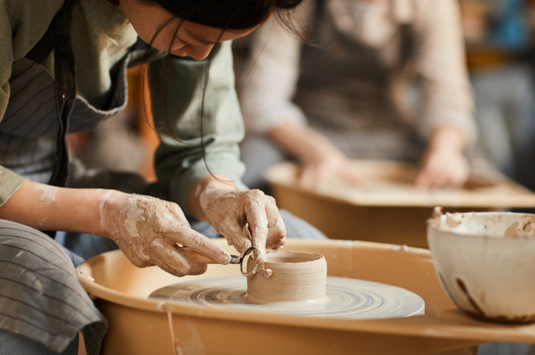 A person is using a tool to cut the top of a pot on a pottery wheel