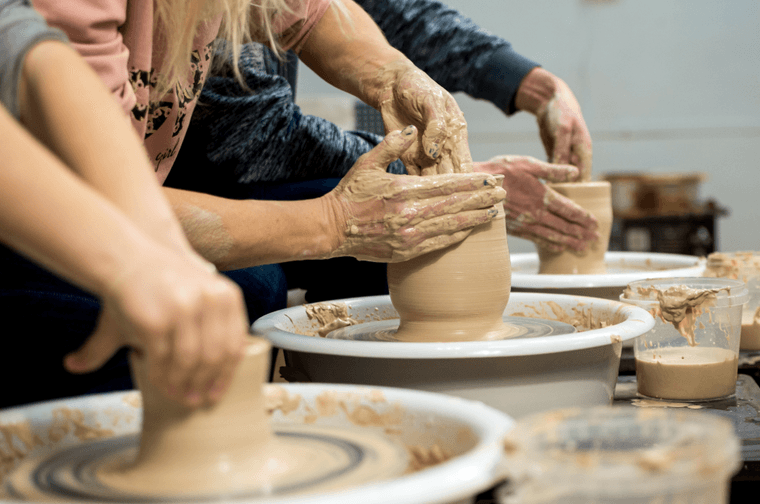 Three people are using a pottery wheel to mould pots