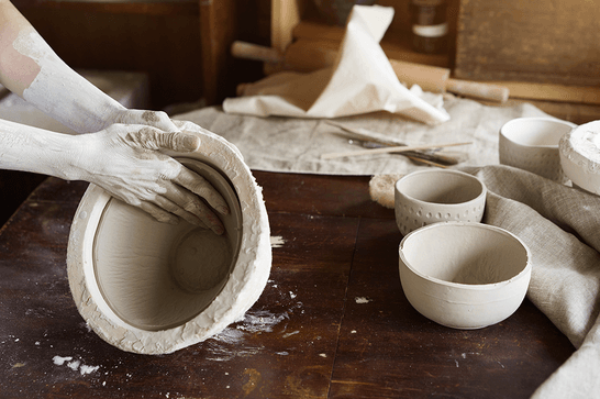 Someone with dry clay on their hands is removing a bowl from a mould
