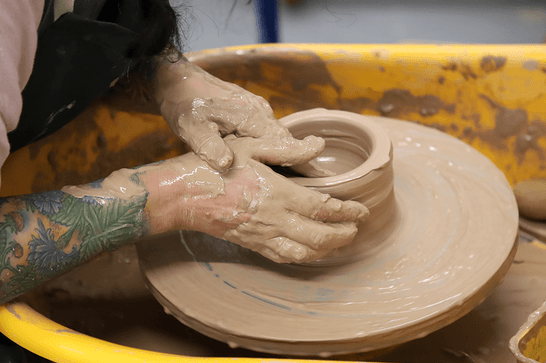 A person's hands are forming clay on a pottery wheel