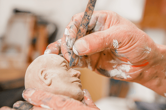 A person is using a tool to sculpt a miniature head out of clay