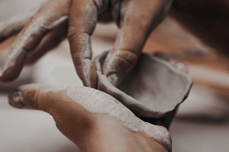 A person is moulding a small bowl from clay with their fingers