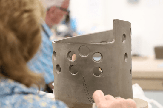 A person is carving into a clay pot with circles cut out of it and an angled top