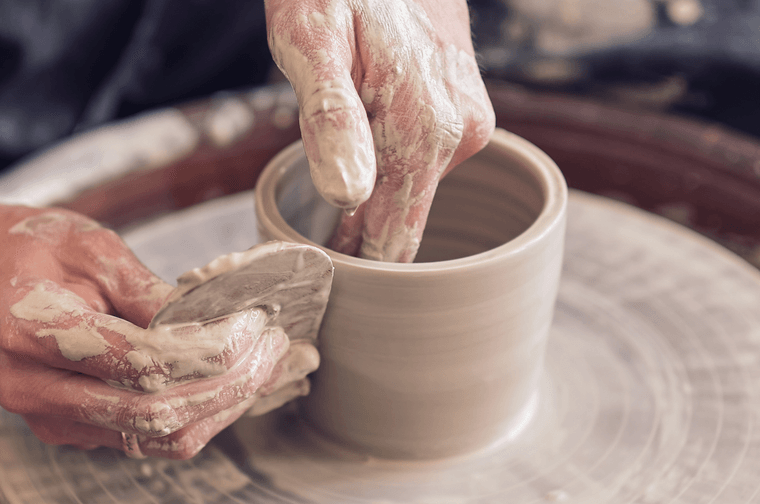 A person is using a tool to smooth the outer edge of a pot that is spinning on a potters wheel