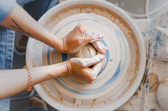 A persons hands are moulding clay on a pottery wheel