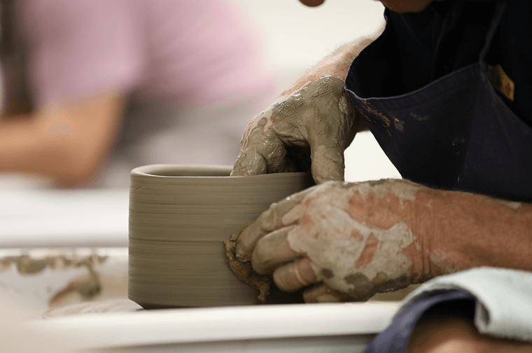 A person's hands are forming clay on a pottery wheel