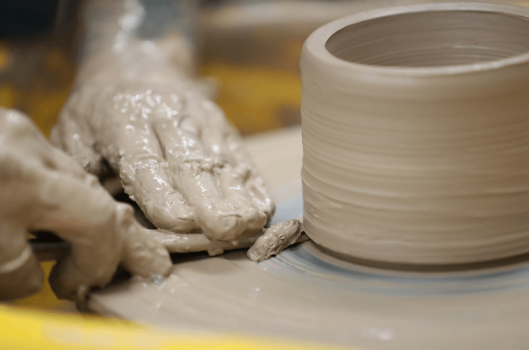 A person is using a tool to shave off bits of a pot on a potters wheel