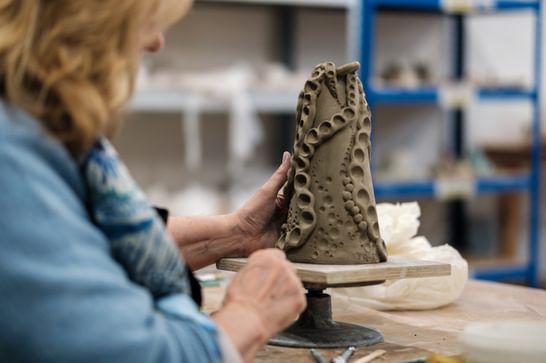 A woman is holding a clay vase, with circular shapes carved from it