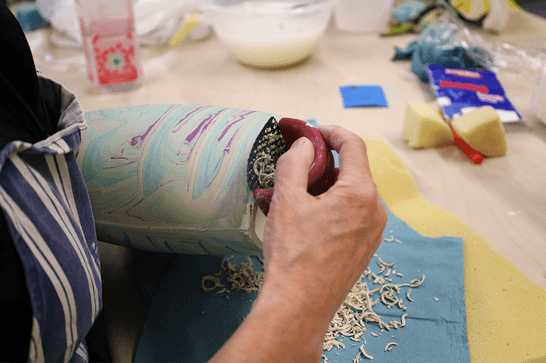 A person is grating a blue and purple marbled pot to make it smooth