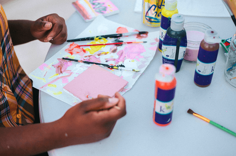 A child is sat at a table, with a range of paints, brushes, paper and glue