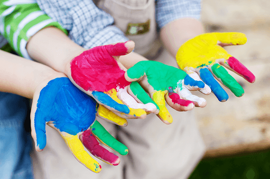 Children's hands being held out, with coloured paints covering their hands