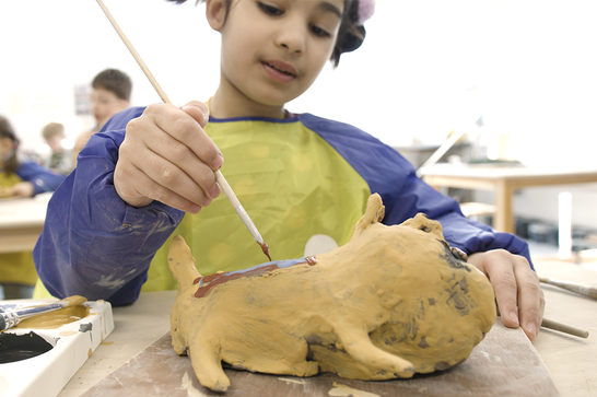 A young child is painting a clay sculpture with yellow paint while smiling