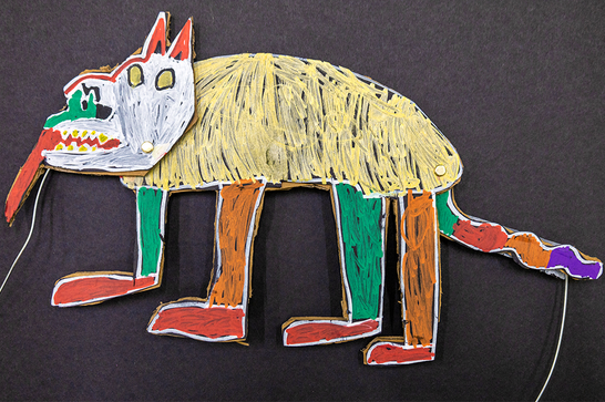 A colourful wolf-like puppet against a black background