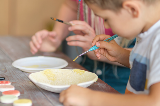 A child is painting a ceramic plate with yellow paint