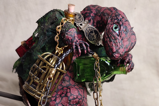 A paper mache lizard creature is covered in chains holding a green bottle