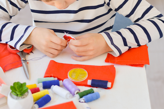 A child in a blue and white stripey top is sewing orange material together
