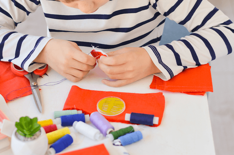 A child in a blue and white stripey top is sewing orange material together
