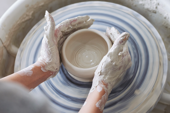 A person is moulding a pot on a pottery wheel