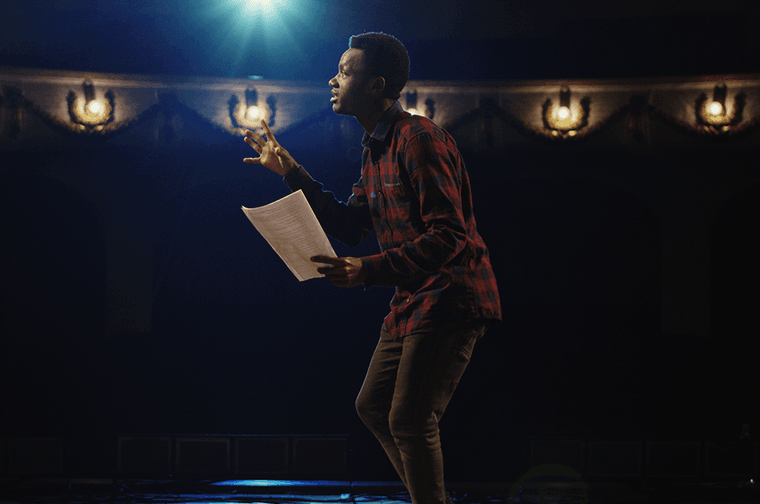 A person is on stage with a spotlight on them, with a paper script in hand