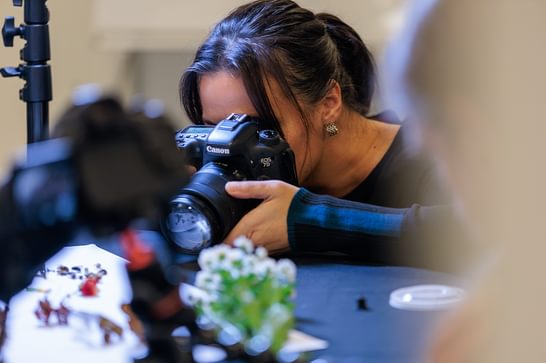 A person is holding a black camera, photographing objects on a black table.