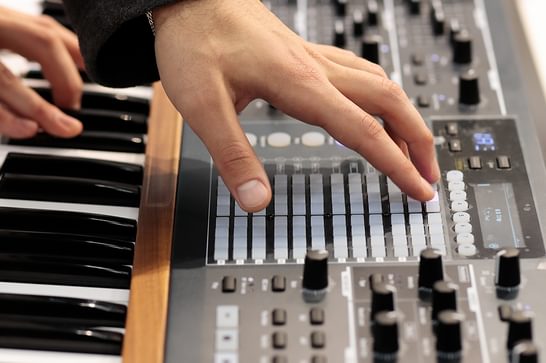 A person's hand is touching buttons on a grey sound board, which has a keyboard connected to the front of the soundboard