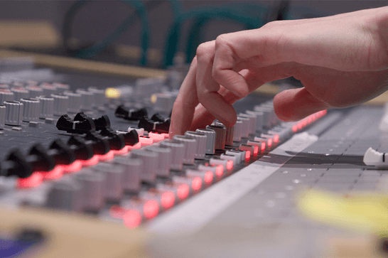 A person's hand is reaching the buttons of a studio recording desk