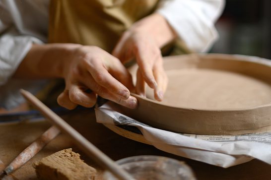 A person moulding a plate with a ridged edge with their hands