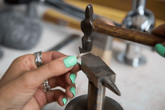 A person is using a hammer to form a silver metal at a workstation