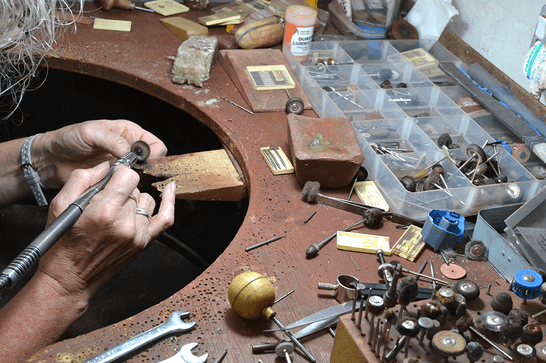 A person is polishing jewellery with a tool, at a workbench filled with jewellery making equipment