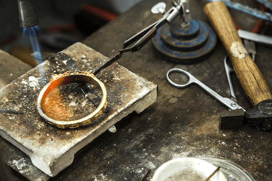 A person is holding a silver bracelet with a tool, using a tool to fire it and heat it up