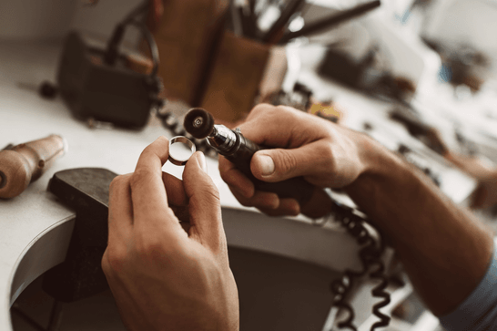 A person is at a workstation, polishing a silver ring with an electric tool