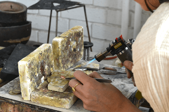 Someone is holding a necklace pendant on a block with tweezers, as they heat it with a flame from the other side