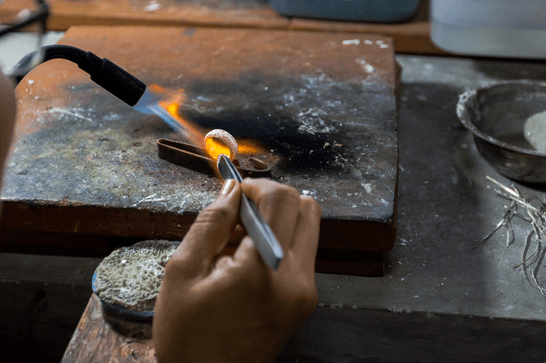 Someone is applying a flame to a ring, holding it in place with jewellery tweezers