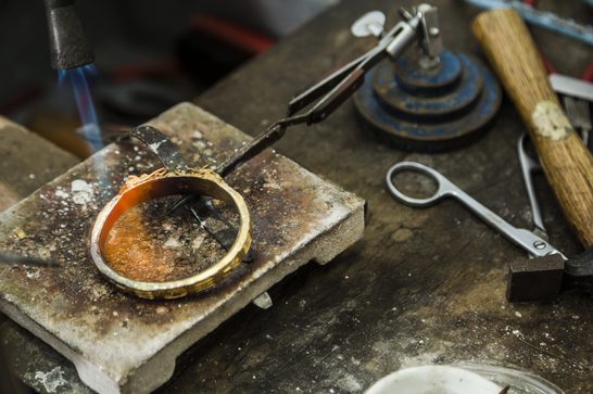 A bright blue flame is above a silver bracelet, turning orange as it makes contact