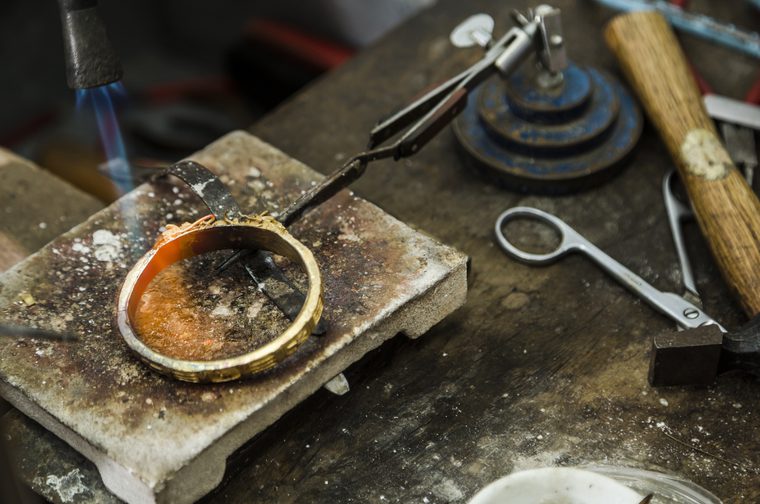 A bright blue flame is above a silver bracelet, turning orange as it makes contact