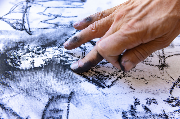A person is drawing a person in charcoal, and using their finger to smudge the lines