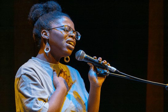 A person is holding a microphone, singing passionately into it with their hand on their chest