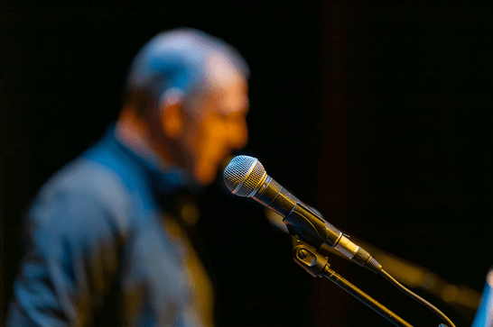 A microphone, and in the background a blurry person is stood aligned to the mouthpiece