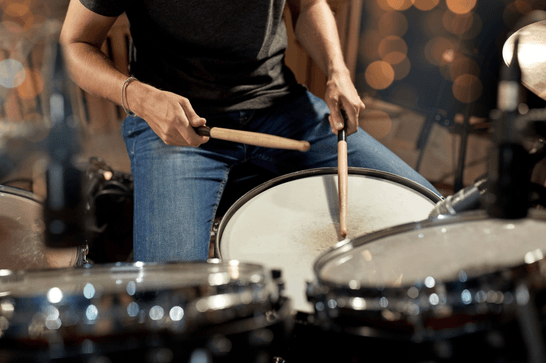 Someone is sitting at a drum kit using the sticks to bang on it