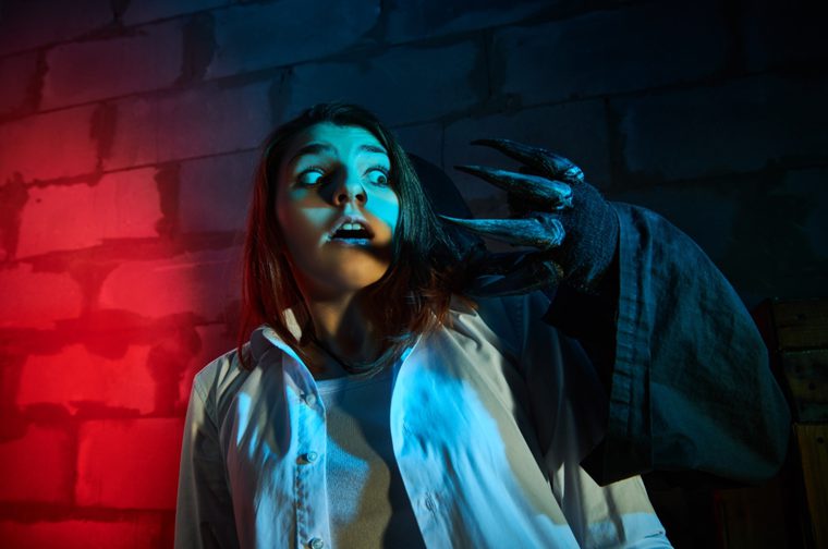 A child is against a brick wall, with a black ghoulish arm reaching towards them. The child had a scared face.