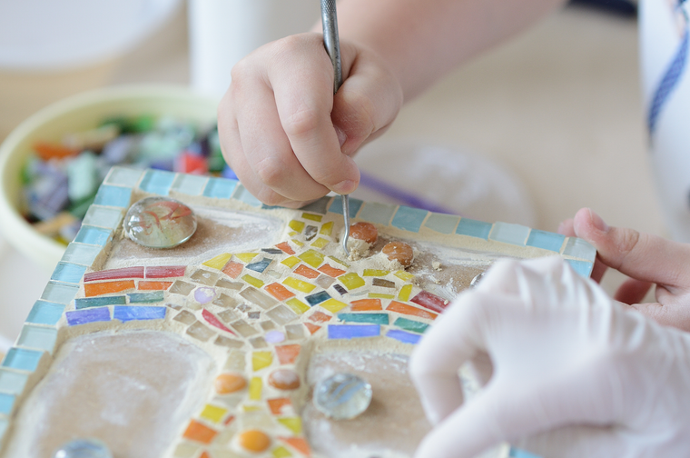 A child is placing tiles to make a mosaic pattern on a wooden board