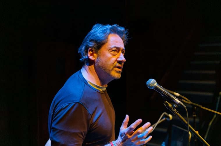 A man in standing at a microphone, singing passionately, with his hand outstretched