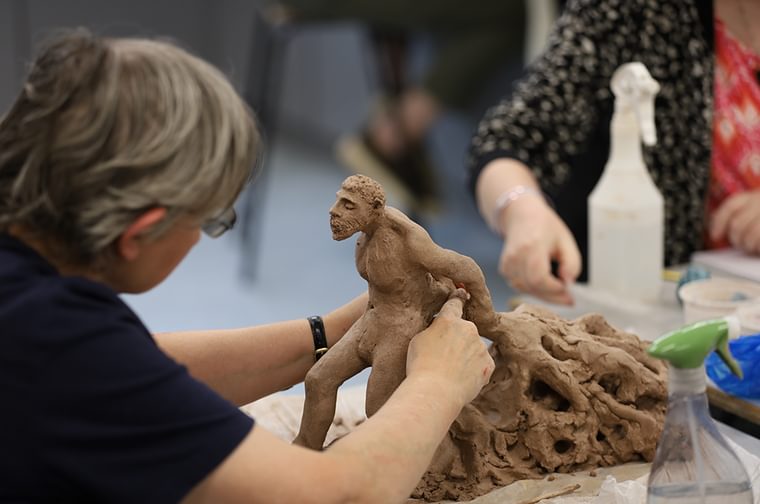 A woman is sculpting clay, forming a man who is connected to roots
