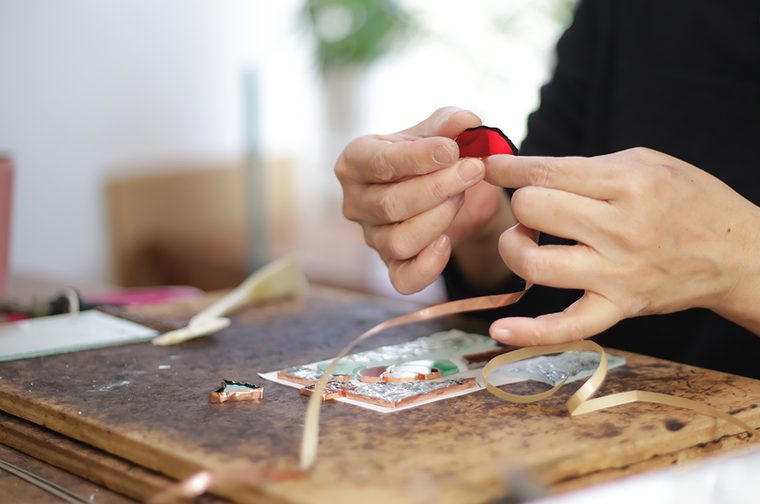 A person is wrapping a piece of red glass with copper.