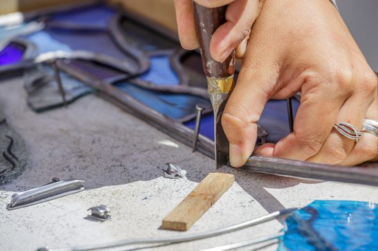 Someone is cutting lead around blue glass, arranged in a nice pattern
