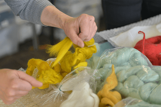 A person is tearing yellow felt, with bags of green and red felt in the background