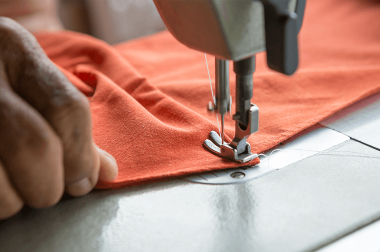 A person is guiding orange fabric through a sewing machine